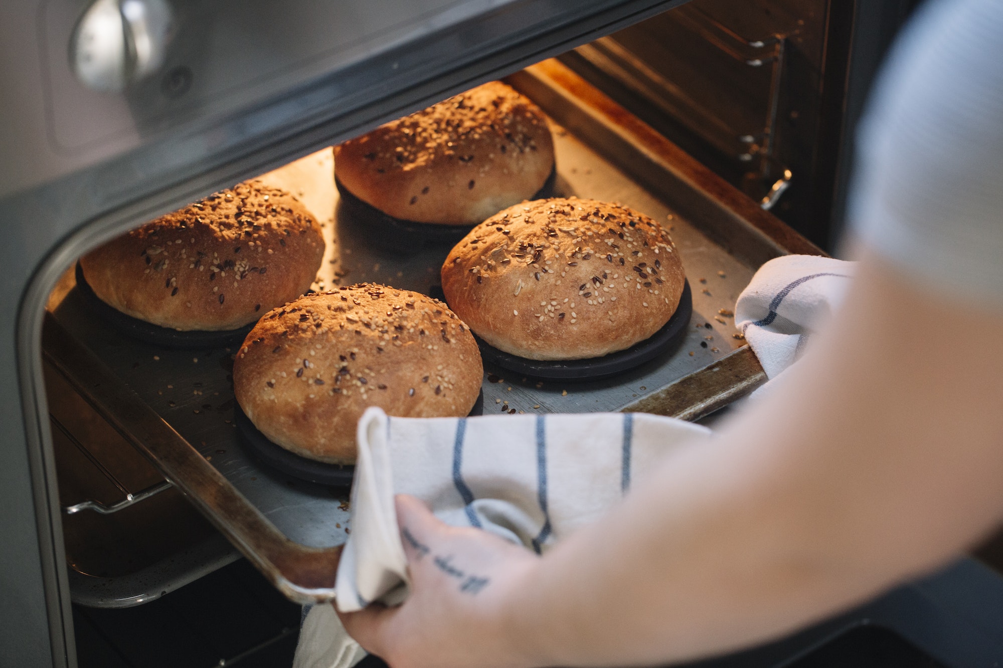 Woman taking homemade vegan burger rolls out of oven
